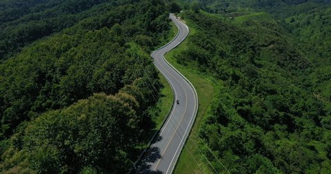 Aerial view of motorcycle driving on country road in forest. Cinematic drone shot flying over country road with curved in the mountain.