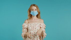 Woman in protective mask applies disinfectant antiseptic to her hands. Stop virus concept, bacteria protection. Blue studio background.