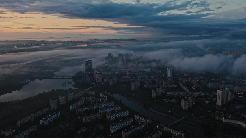 Aerial panoramic view of dark city after rain and sunset. Cloudy sky, smog, picturesque riverscape and tenement buildings. Evening traffic. Slow motion, cinematic