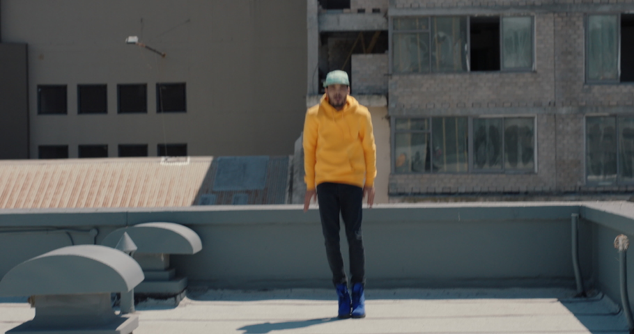 dancing man hip hop dancer performing freestyle dance moves on rooftop in city wearing yellow hoodie