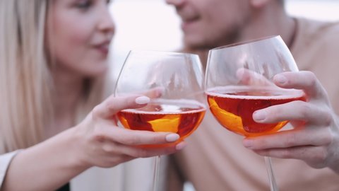 Romantic date concept. Man and woman having a picnic at the bay. They are holding glasses with sangria cocktail, focu on glasses with orange inside.