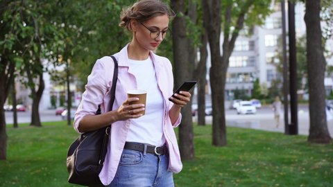 Businesswoman standing summer park Business person using smartphone Outdoors Successful european caucasian woman freelancer or teacher walking outside backpack dressed jeans white shirt pink jacket
