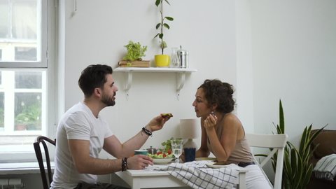 woman and bearded man husband feeding sharing food with lovely. cute couple eating together in kitchen. pretty wife girlfriend biting meal sandwich. concept love, marriage