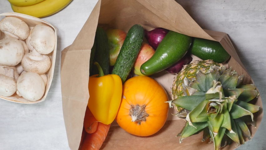 Top closeup view of woman hand put fruits and vegetables into cardboard bag. Healthy food home delivery concept