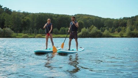 Smiling man and woman standing on sup board and swims surfing on the lake with a paddle for swimming rowing sport surfer friends close up slow motion
