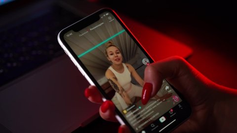 MOSCOW, RUSSIA, 20 OCTOBER 2020 .Woman's hand with red manicure holding iPhone with streaming service media and video TikTok on the screen.