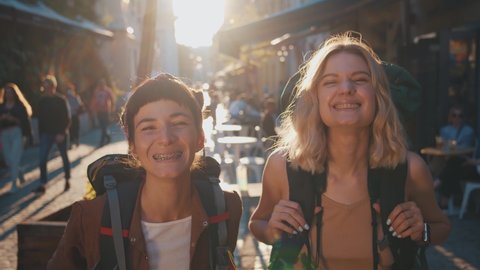 Couple portrait of funny caucasian two travel women with backpacks smiling into camera showing teeth with braces having fun laughing. Tourists.