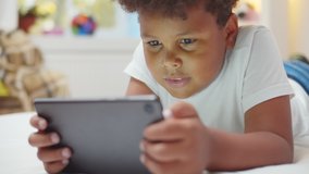 Afro-american boy kid lying on bed watching cartoons on digital tablet. Close up portrait of adorable african child playing game on tablet pc relaxing in bedroom at home - Powered by Shutterstock - Get 15% off with code: PIKWIZARD15