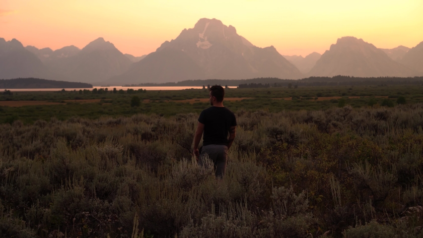 A young adult stands in a clearing before the Grand Tetons in Wyoming.