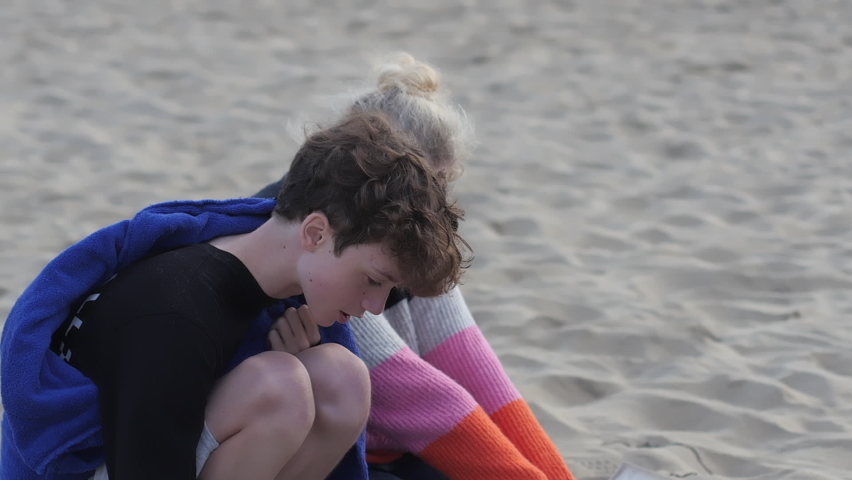 Mother and son close together snug on a beach talking and sharing, slow motion