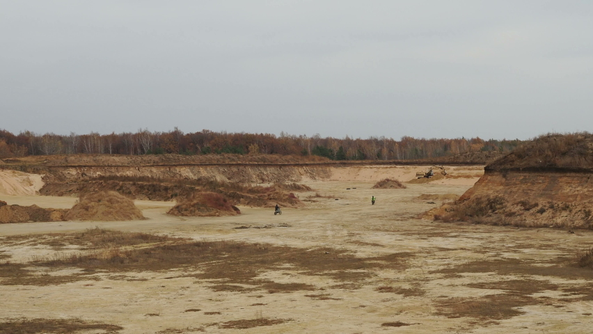 two motorcyclists ride on a sandy off-road and jump over a small hill.