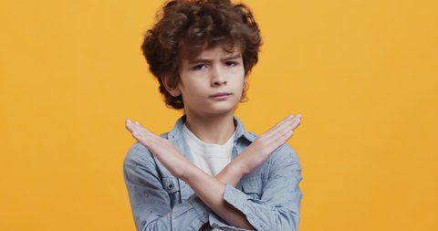 Stop children abuse. Cute curty boy gesturing no, crossing hands and shaking head, expressing reject and denial, orange studio background