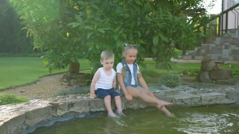 outdoors games, barefoot children wet their feet while playing with water in a pond sitting together in the park
