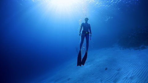 Woman freediver ascends from depth in bifins