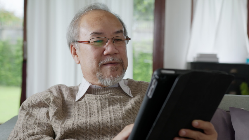 Candid of old asian retired man using tablet computer to transfer money online or financial payment and read text, smile or laugh with happy and positive. Senior asian with digital technology concept | Shutterstock HD Video #1061038840