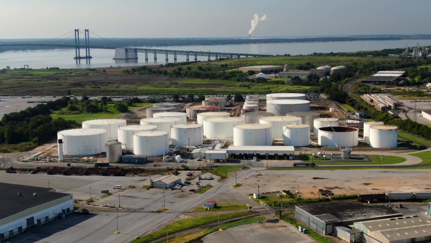 Aerial of oil and gas fuel refinery storage tanks at Wilmington USA port, Delaware Memorial Bridge in distance. Tractor trailer truck arrives to pick up load of gasoline or diesel for distribution. Royalty-Free Stock Footage #1061039218