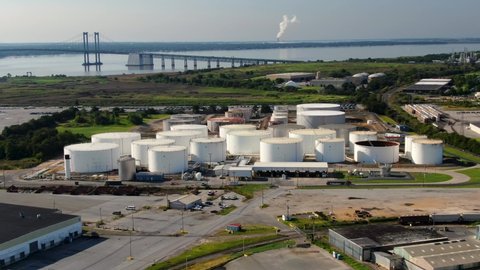 Aerial of oil and gas fuel refinery storage tanks at Wilmington USA port, Delaware Memorial Bridge in distance. Tractor trailer truck arrives to pick up load of gasoline or diesel for distribution.