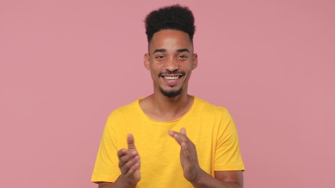 Smiling funny young african american man 20s years old in yellow t-shirt posing isolated on pastel pink background in studio. People lifestyle concept. Looking camera applause cheering clapping hands