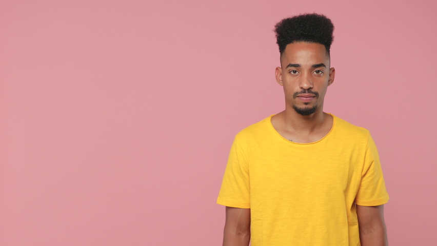 Surprised young african american man 20s years old in yellow t-shirt posing isolated on pink background studio. People lifestyle concept. Looking camera pointing index finger aside showing thumb up Royalty-Free Stock Footage #1061042701
