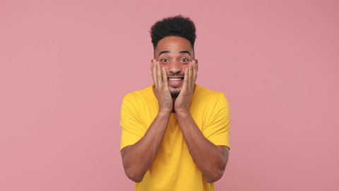 Side profile view of surprised young african american man 20s in yellow t-shirt posing isolated on pink background in studio. People lifestyle concept. Turn around camera say wow doing winner gesture