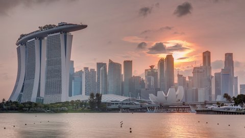Sunset over the downtown skyline of Singapore as viewed from across the water from The Garden East timelapse. Sun behind skyscrapers. Singapore. Reflection in water