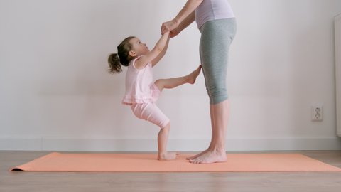 Young adult mother doing exercises with little baby girl at home