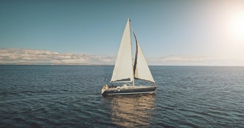 Sailing yacht race at sun light aerial. Yachting on serene seascape at open sea. Boat with big white spinnaker sail at ocean bay. Lonely ship cruise at water on summer sunny day. Cinematic drone shot