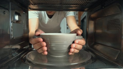 The man puts a bowl of food to warm in the microwave. inside camera.