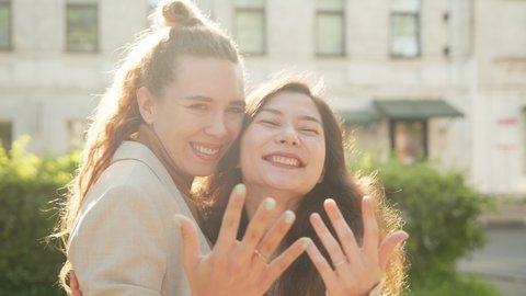 Happy lesbian couple posing for photohrapher. Girls showing engagement rings on hands enjoying romantic celebration. Together taking selfie, extremely happy. LGBT Pride Month, Gay Pride Symbol