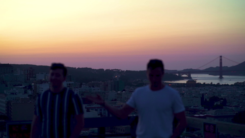 Out of focus men on a roof, in front of the Golden gate bridge, during dusk, in San Francisco, California, USA - Pan shot