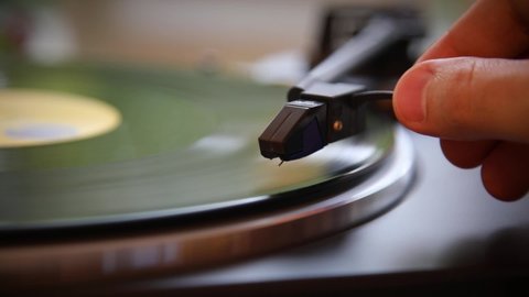 Hand turns on a vintage vinyl record. The needle rises from a vintage vinyl record. The vinyl record is spinning. The needle plays on a vintage vinyl record. Old turntable.