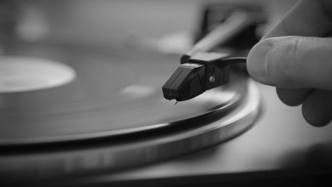 Black and White. Hand turns on a vintage vinyl record. The needle rises from a vintage vinyl record. The vinyl record is spinning. The needle plays on a vintage vinyl record. Old turntable.