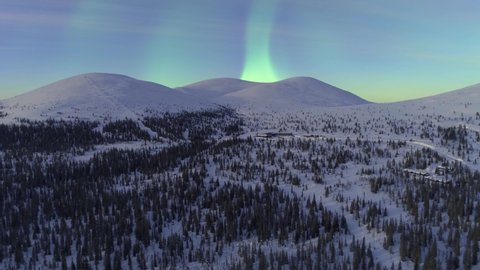 Aerial, drone shot towards Aurora Borealis, the Northern lights above the Pallastunturit mountains, in Pallas-yllastunturi national park, winter dawn, in Muonio, Lapland, Finland