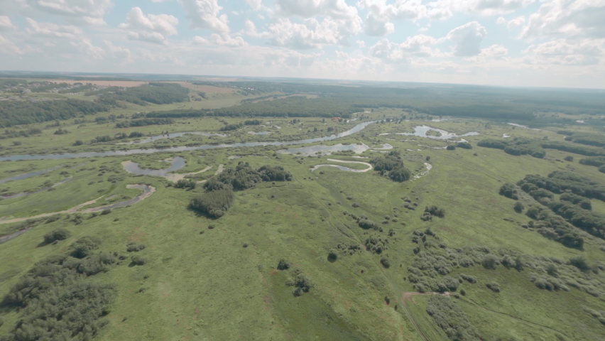 Large eagle flies over wide valley with curved river and mirror lake against sky with fluffy clouds first point fpv sport drone follow view
