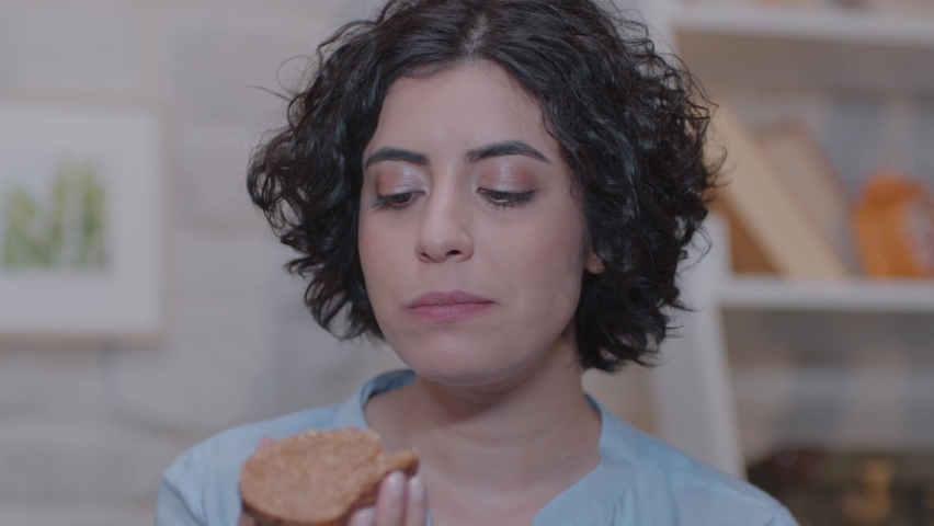 Young woman is sitting on an armchair at home and eating peanut butter bread. Royalty-Free Stock Footage #1061073331