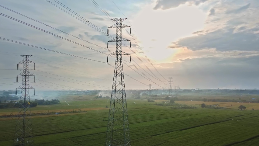 Aerial drone view of a newly constructed electric transmission tower on a green rice field at the sunset | Shutterstock HD Video #1061074903