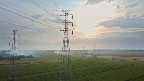 Aerial drone view of a newly constructed electric transmission tower on a green rice field at the sunset