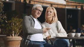 Cheerful smiling aged couple relaxing and hugging at outdoor cafe table. Portrait of romantic aged man and woman drinking coffee and embracing on restaurant terrace - Powered by Shutterstock - Get 15% off with code: PIKWIZARD15