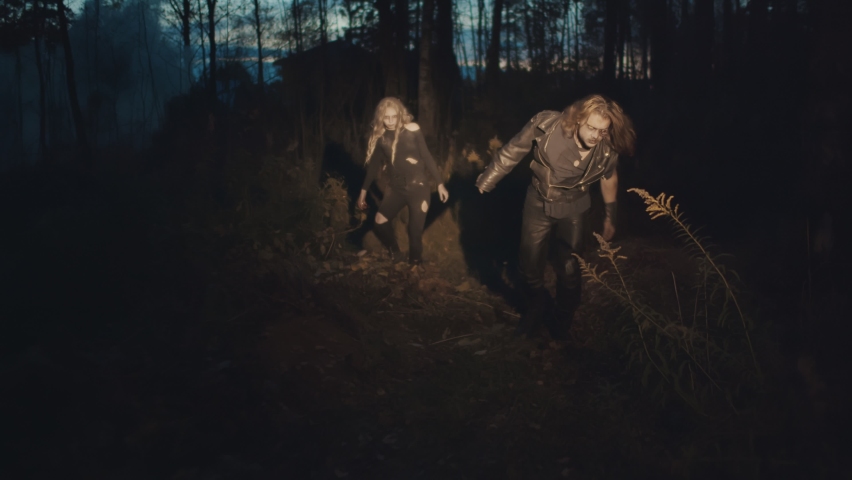 Flashlight illuminating terrible couple zombie walking in night forest. Spooky undead monsters crawling in dark woods. Apocalypse and halloween concept