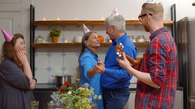 Happy elderly couple dancing in kitchen with young son playing guitar and daughter watching celebrating together wedding anniversary. Family in paper caps at home party - Powered by Shutterstock - Get 15% off with code: PIKWIZARD15