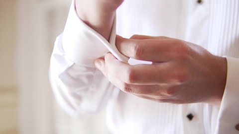 The groom is buttoning his buttons of shirt before the wedding ceremony.