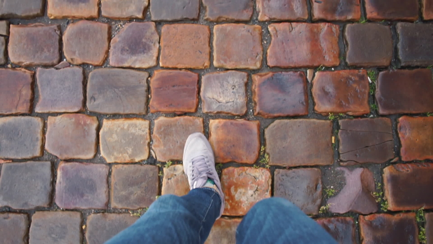 Using navigation in a tourist walk. Legs of a tourist who is lost are walking on wet cobblestones. Orientation on ground. Finding the right direction without the help of electronic navigation. 