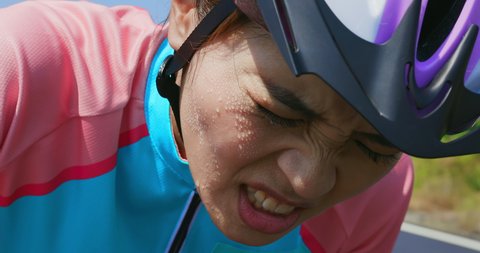 Slow motion of asian young woman wear helmet cycling a bicycle on the road and feel painful