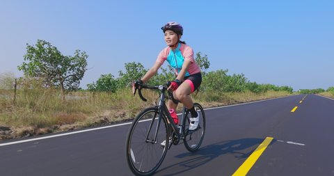 Slow motion of asian young woman wearing helmet is riding a bicycle on the road and enjoy sport or healthy lifestyle concept