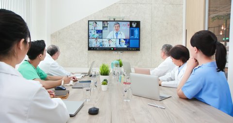 asian old man doctor chatting to medical team using online video chat on tv screen discussing about their thoughts and studies