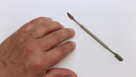 A man's hand lies on the table, next to it is a metal scraper. He wiggles and taps his fingers. Isolated video on a white background. Close-up. Warm, soft light. UHD.