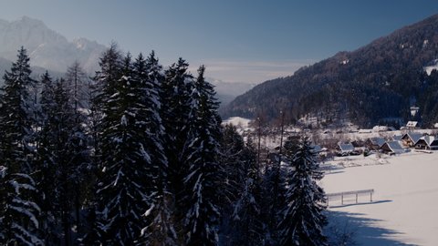 Revealing drone video of alpine village in winter time covered with snow and mountains in background