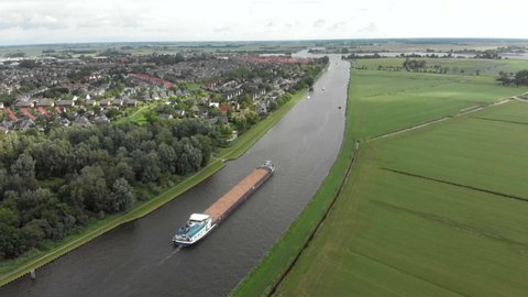 A cargo ship filled with sand is passing by Grou on a cloudy day. Cinematic Drone Aerial in 4K side panning shot