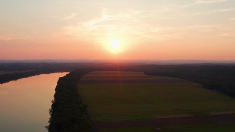 Farmland surrounds the Potomac river as a drone flies over during orange sunset aerial