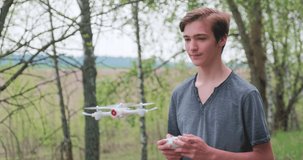 Boy lifts the drone using the remote control. Teenager launches a drone in the open air.  Young man plays with a quadrocopter in nature. White boy learns to fly a drone in a Park. Slow motion video.